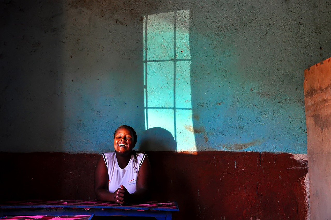 A woman laughing while sitting in front of a wall near light cast through a window