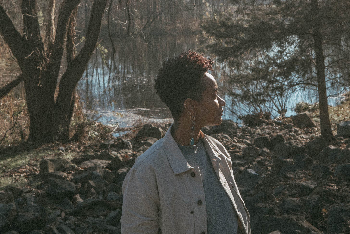 Woman looking off to the side while standing with her back facing a lake