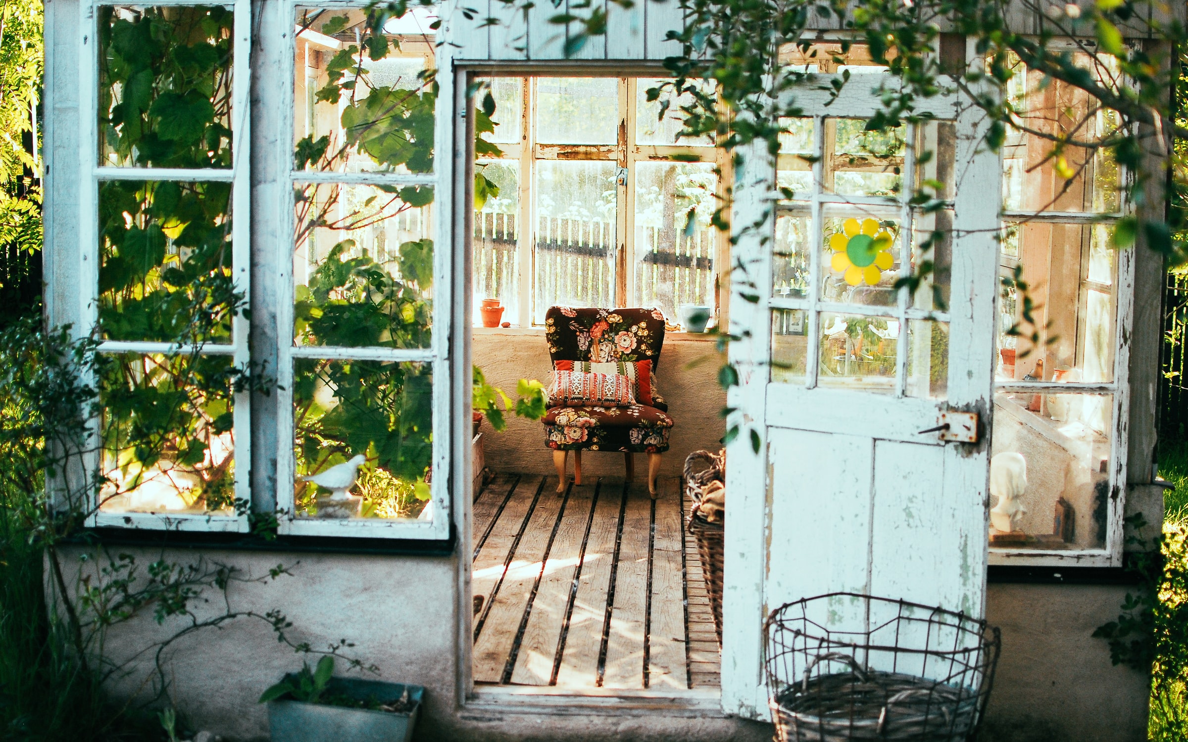a small white garden house covered in green vines with an open door framing a patterned brown chair