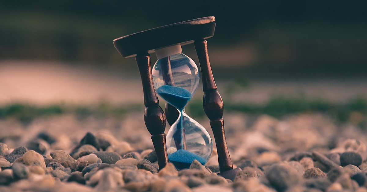 a wooden hourglass sits in the sand with blue sand slowly trickling from top to bottom