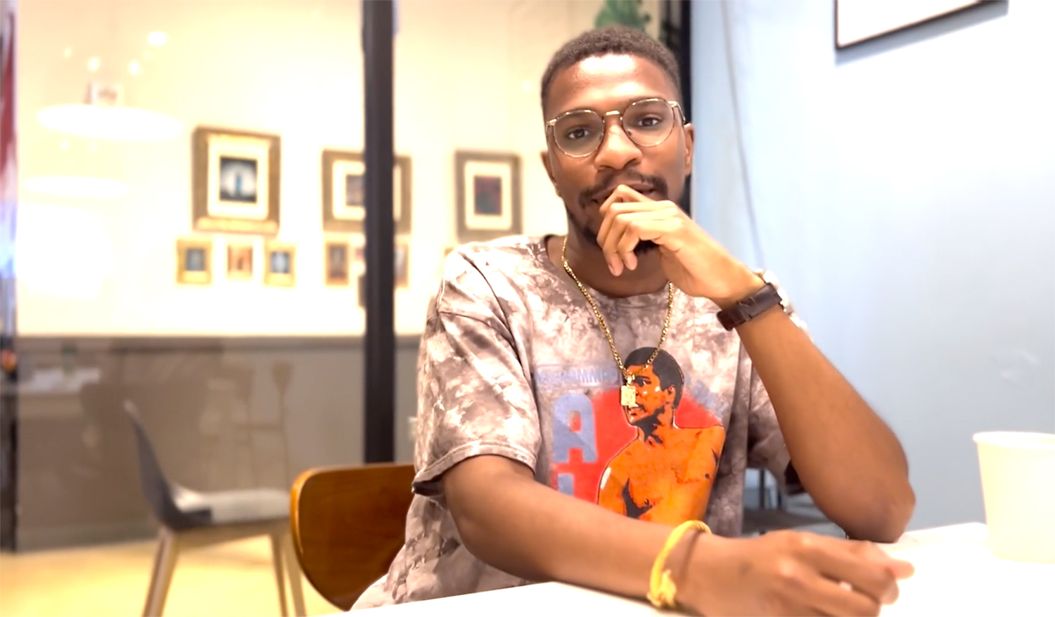 Young Black man sitting in a meeting room with his hand resting near his chin in a casual posture.