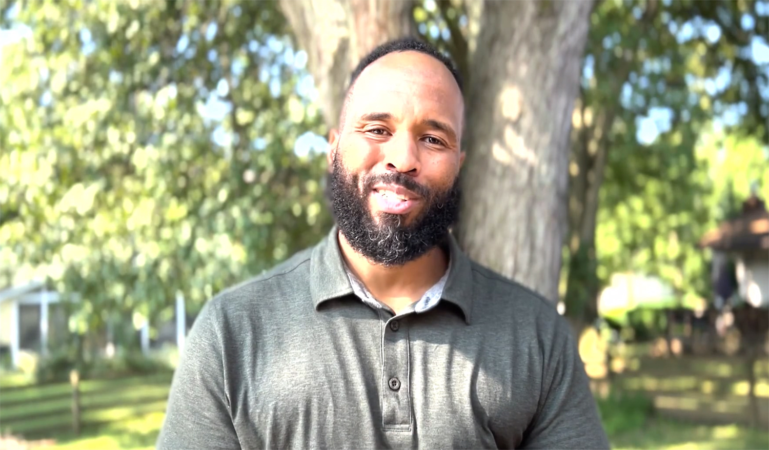 Headshot of a Black man standing outside under the share of a tree