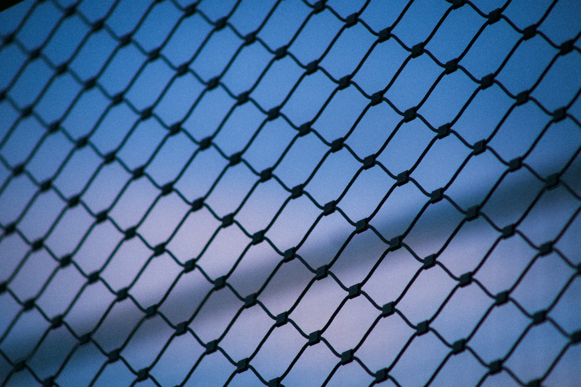 A chainlink fence silhouetted against a dark blue sky