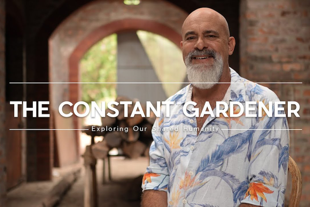 Man sitting in front of a brick archway with text that reads "The Constant Gardener"