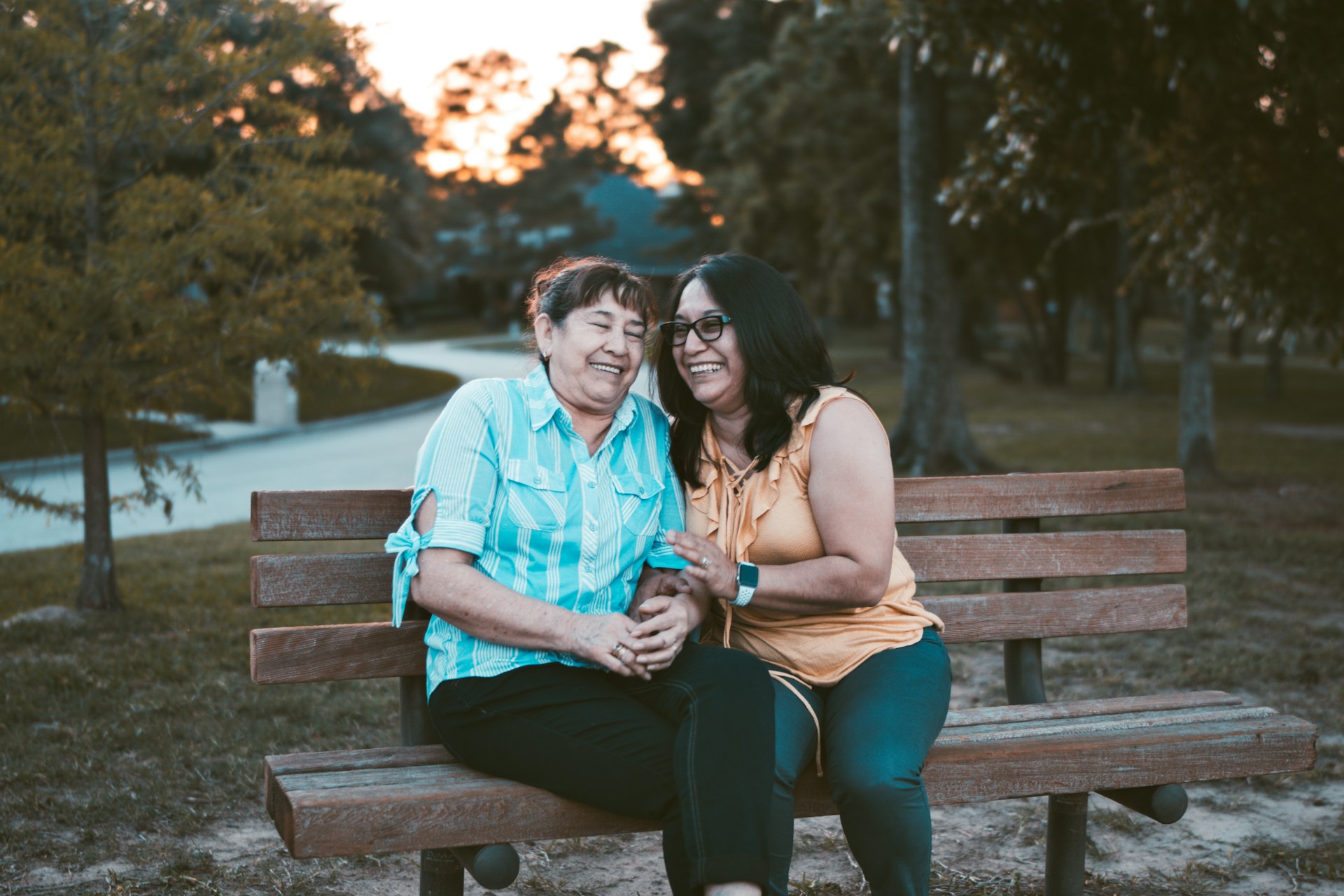 two women smiling and embracing on a bench