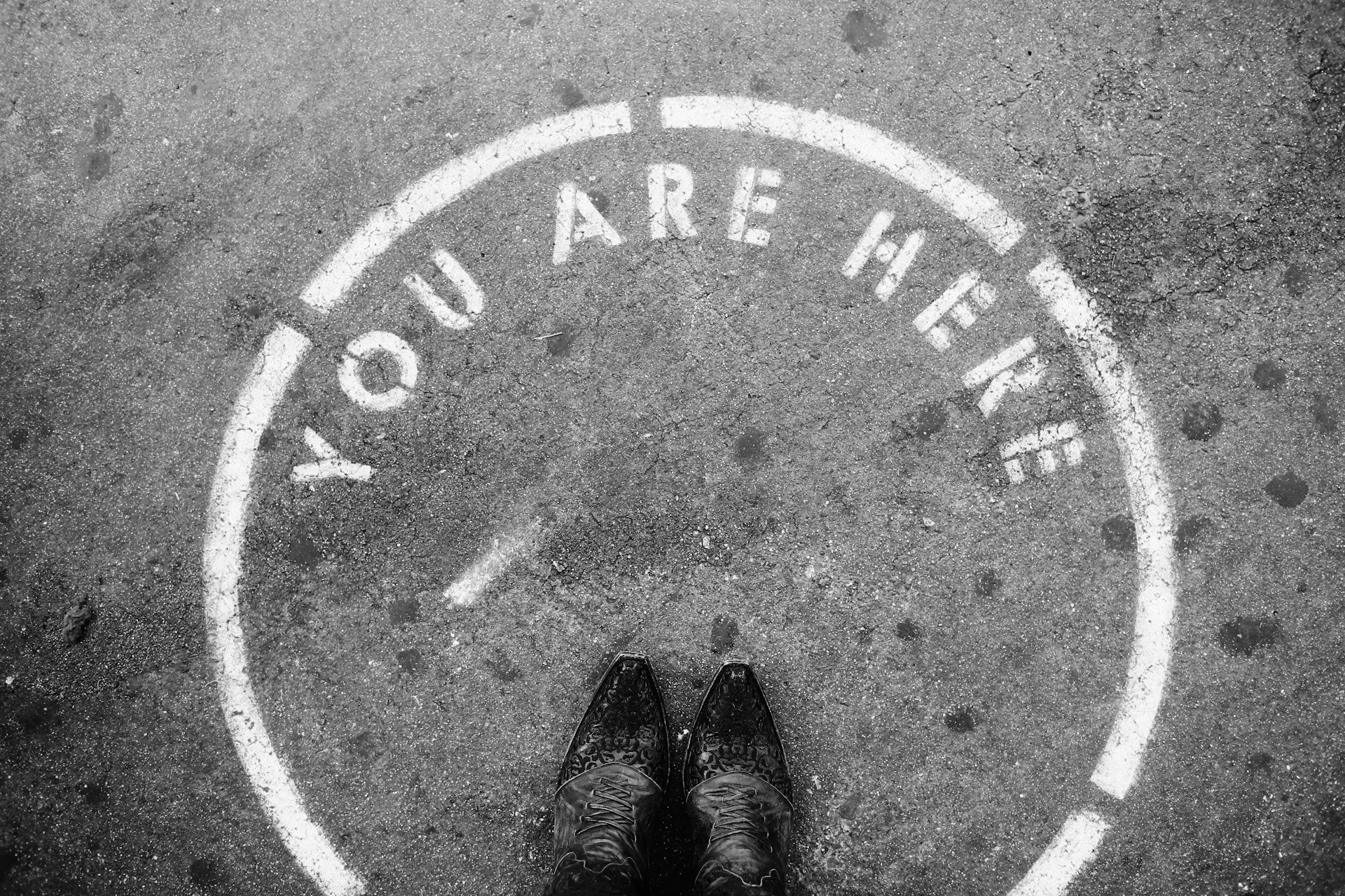 Person standing inside of a circle painted on pavement that says You Are Here