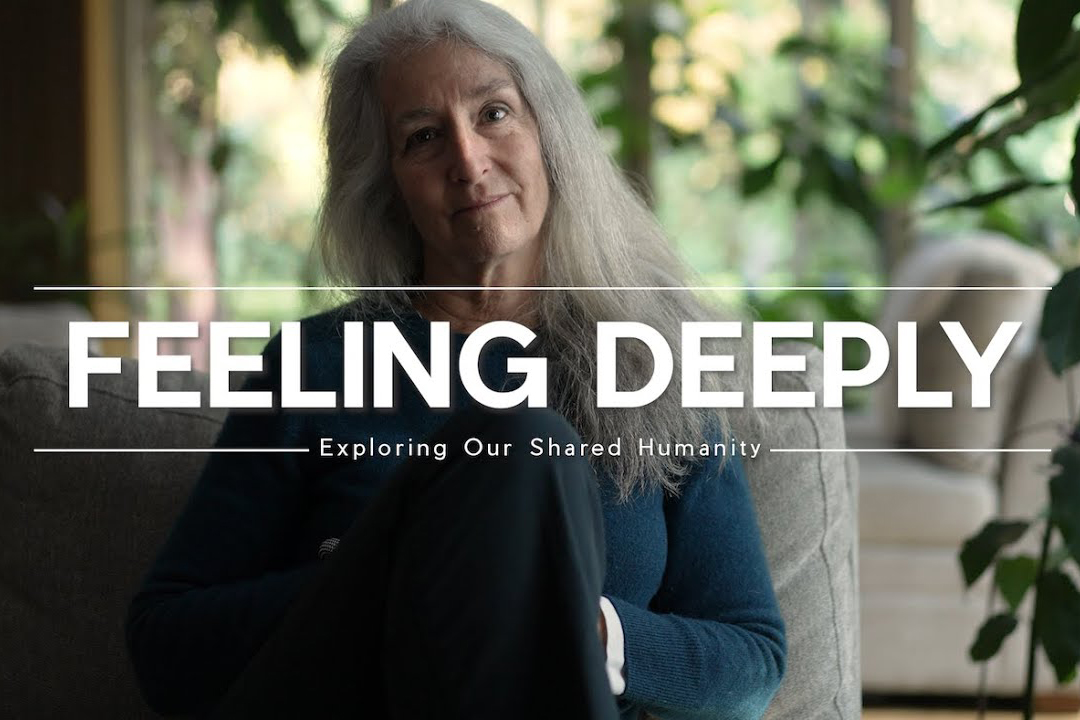 A woman with long grey hair sitting on a sofa with greenery in the background and text that reads, "Feeling Deeply"
