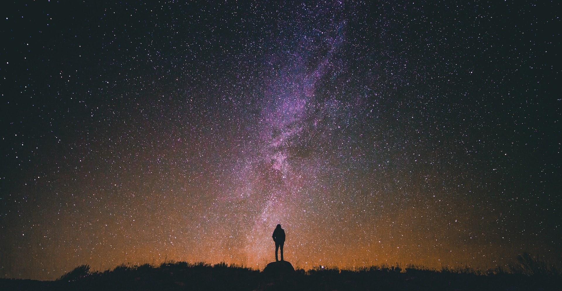 Silhouette of a person standing on a rock looking up at a night sky full of stars