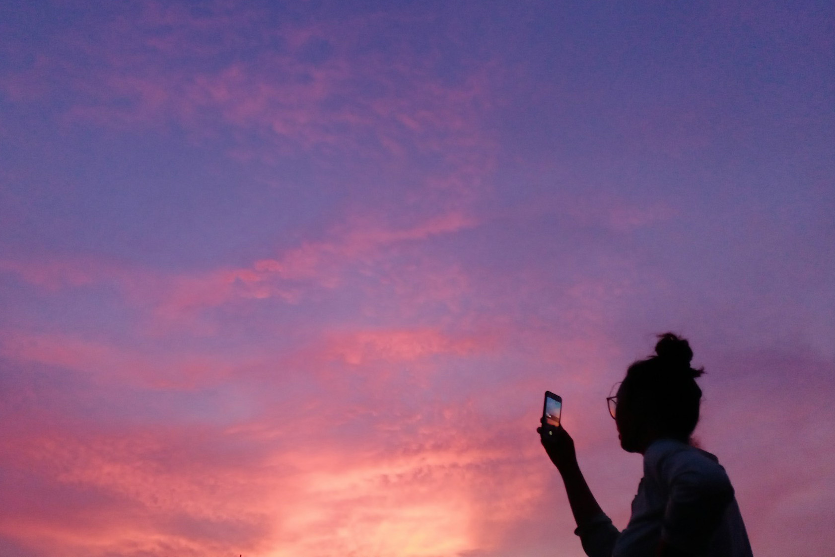 Woman photographing the sunset through her cellphone