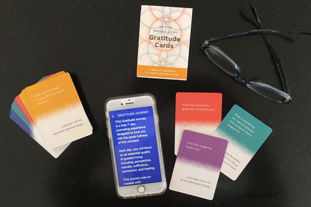 Arrangement of gratitude reflection cards, phone, and glasses on black background