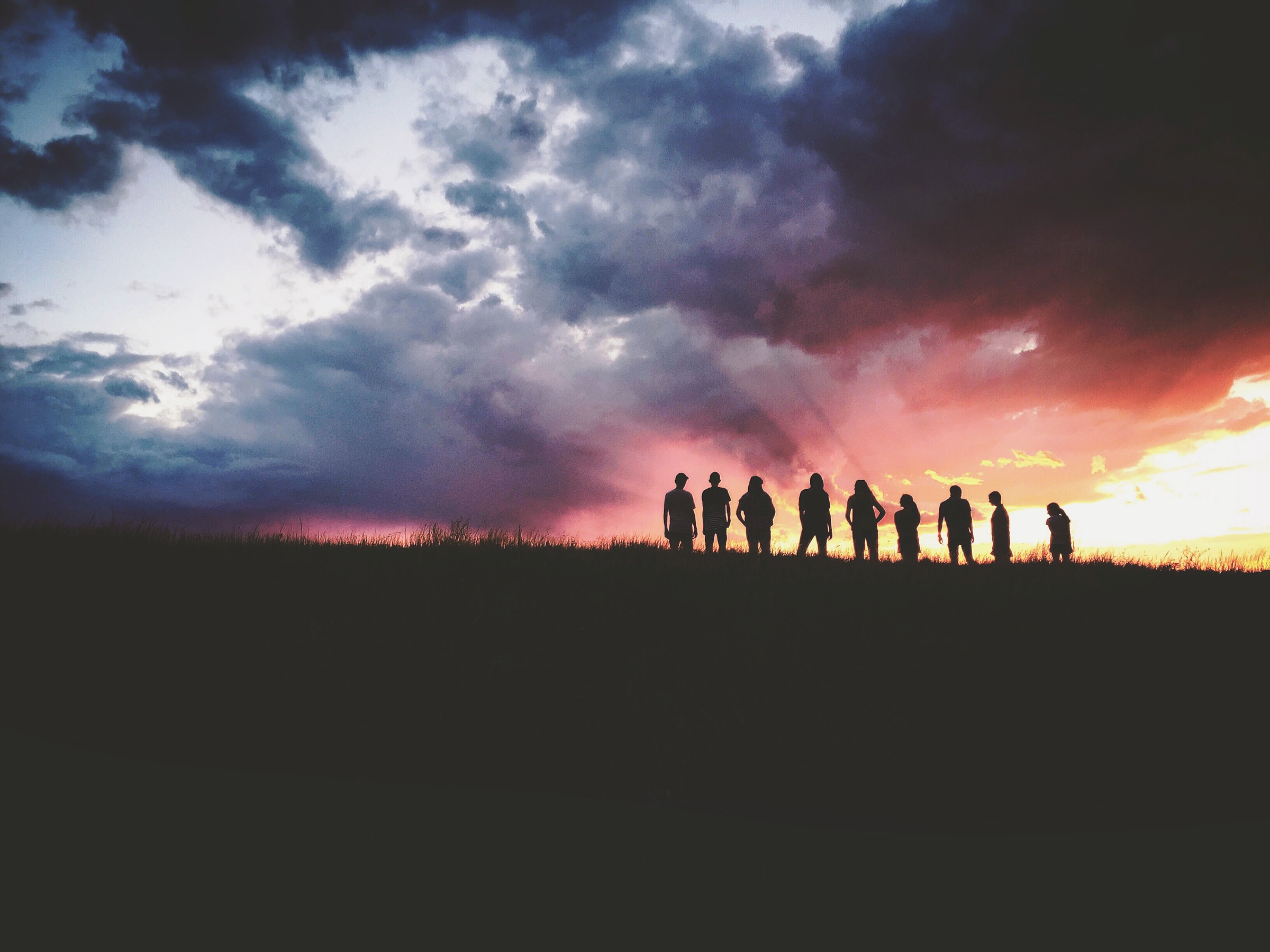 Group of people silhouetted on a hillside against pink and deep purple sunset