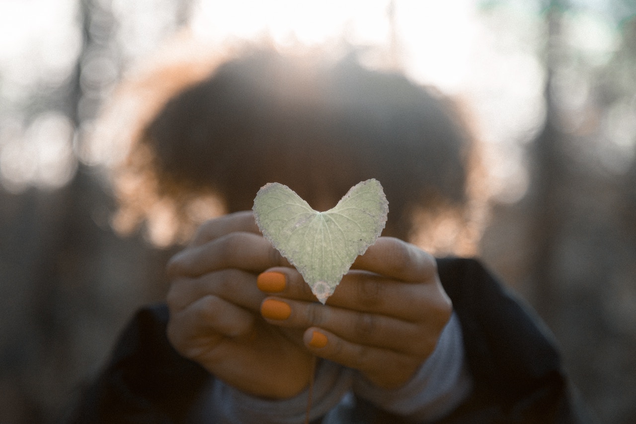Woman extending her hands holding a heart-shaped leaf.
