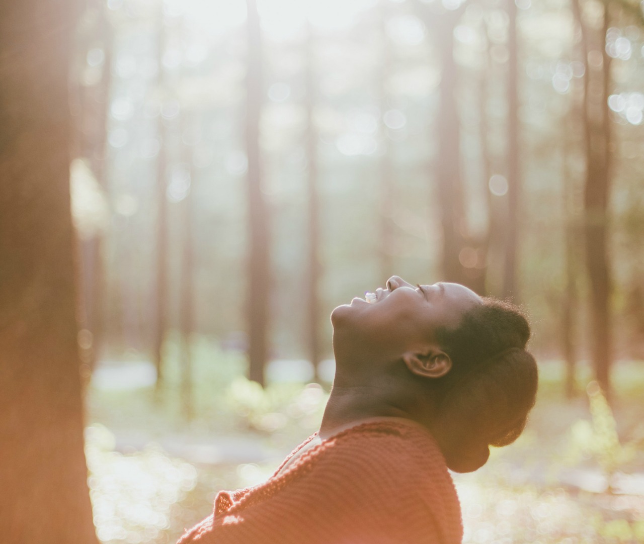 A woman with a ecstatic smile lifts her head to the sky. Forest.