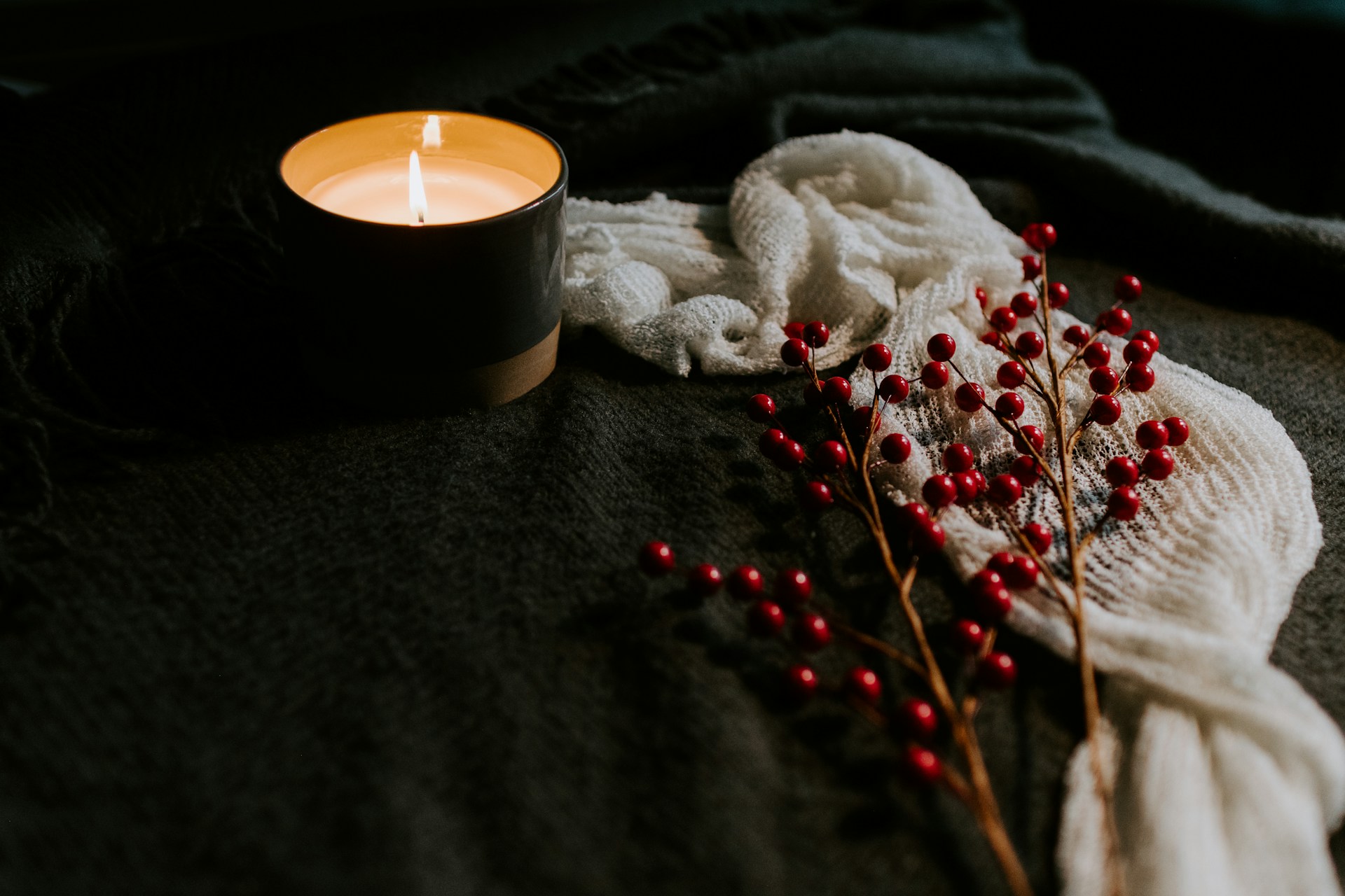 Single candle on a table with soft fabrics and red berries