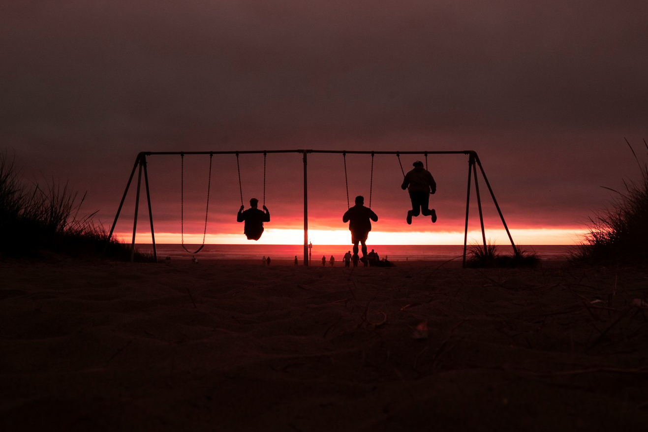 Three people on a swings silhouetted against a red sunset