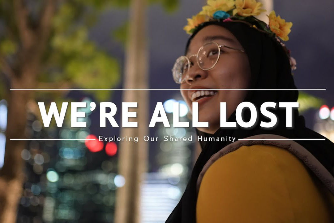 Young woman looking over her shoulder and smiling with text that reads "We're All Lost - Exploring Our Shared Humanity"