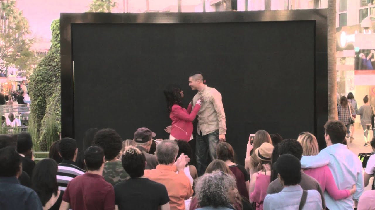 Two people embracing in front of a black screen in front of a crowd of people