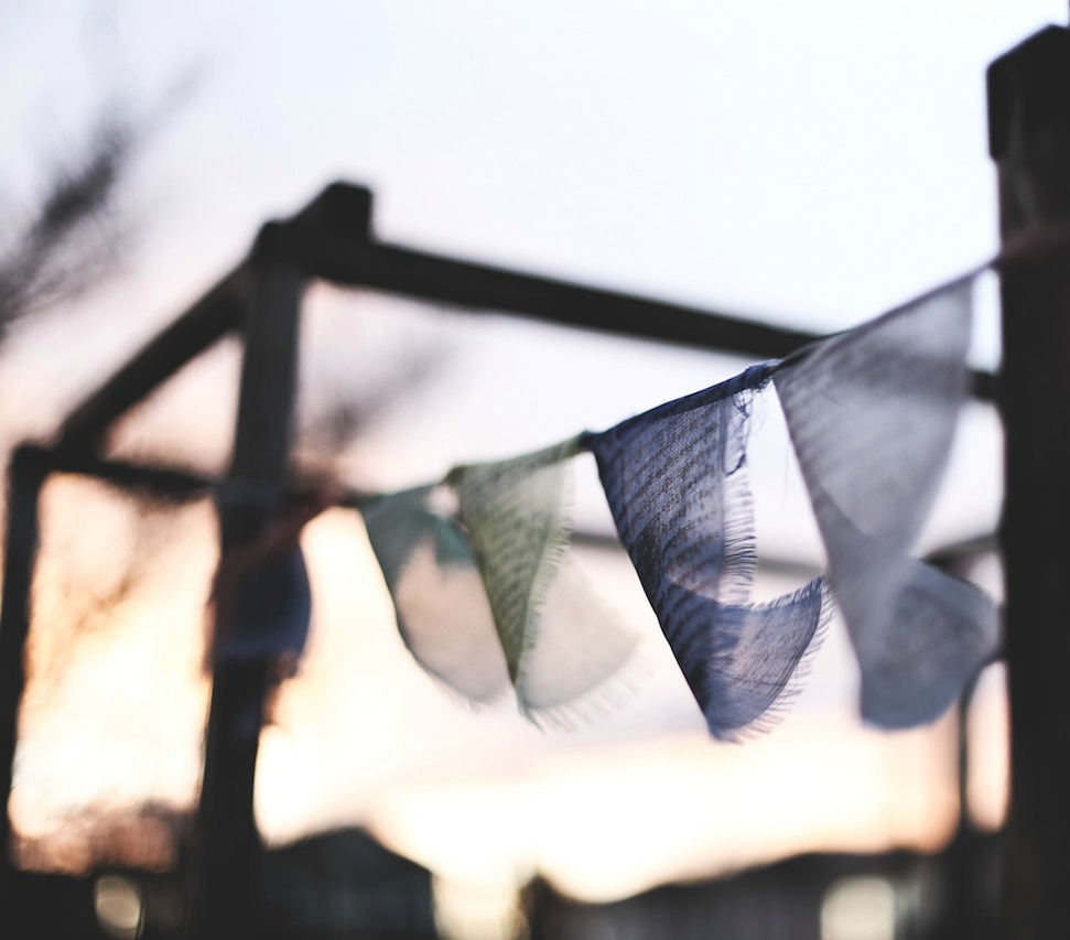 soft-focus photo of prayer flags blowing in a gentle breeze at dawn