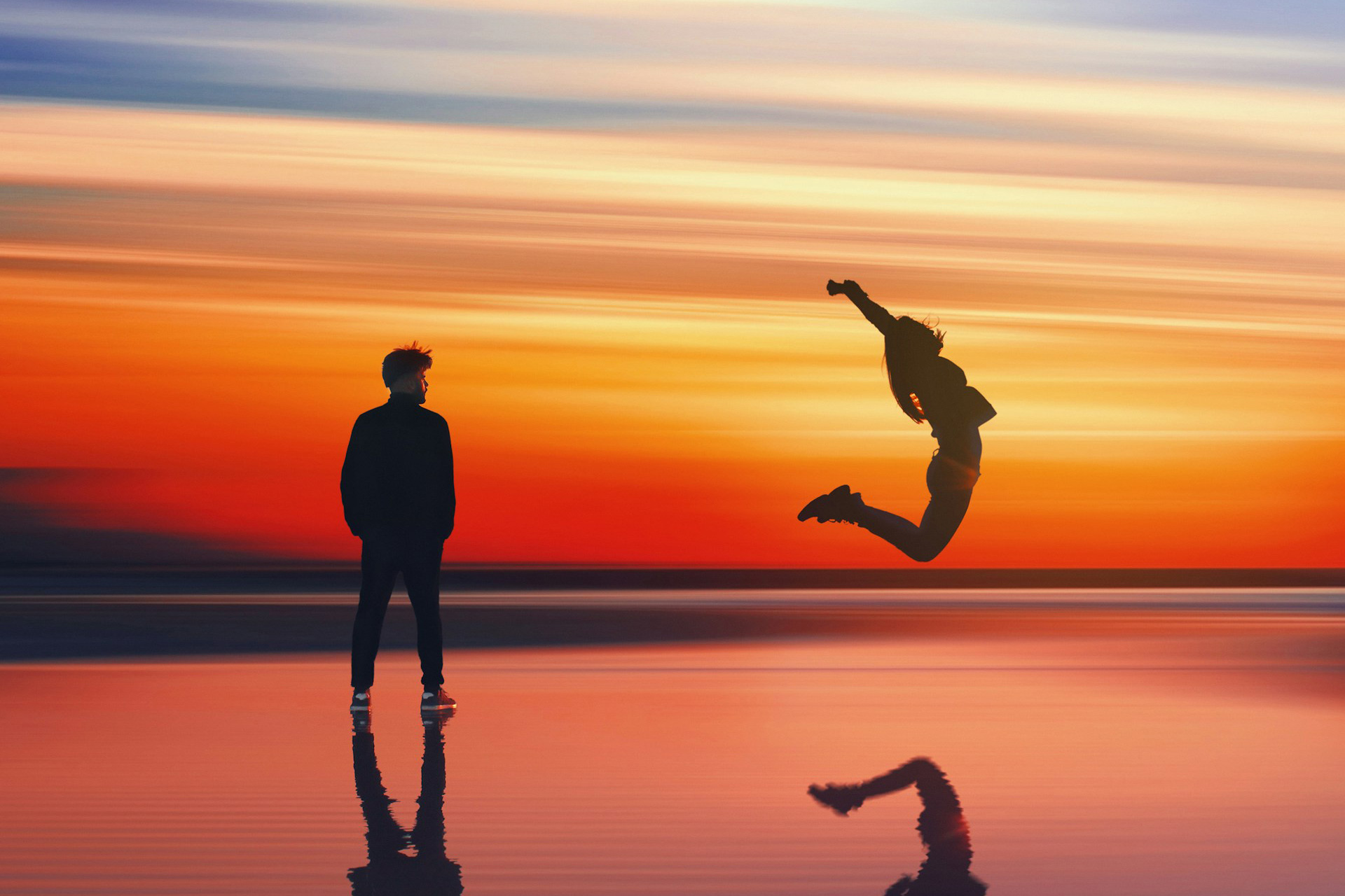 Man standing still looking at a woman jumping joyfully into the air