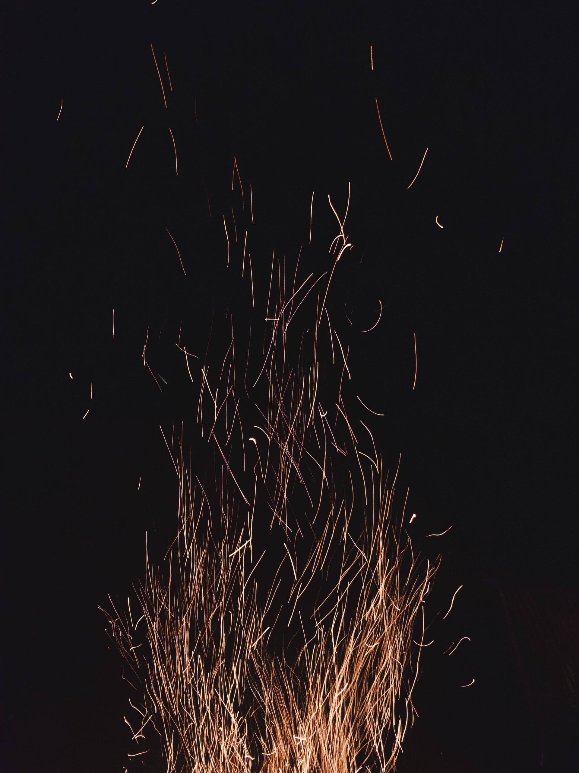 large cluster of sparks from a bonfire rising upward against a dark black background