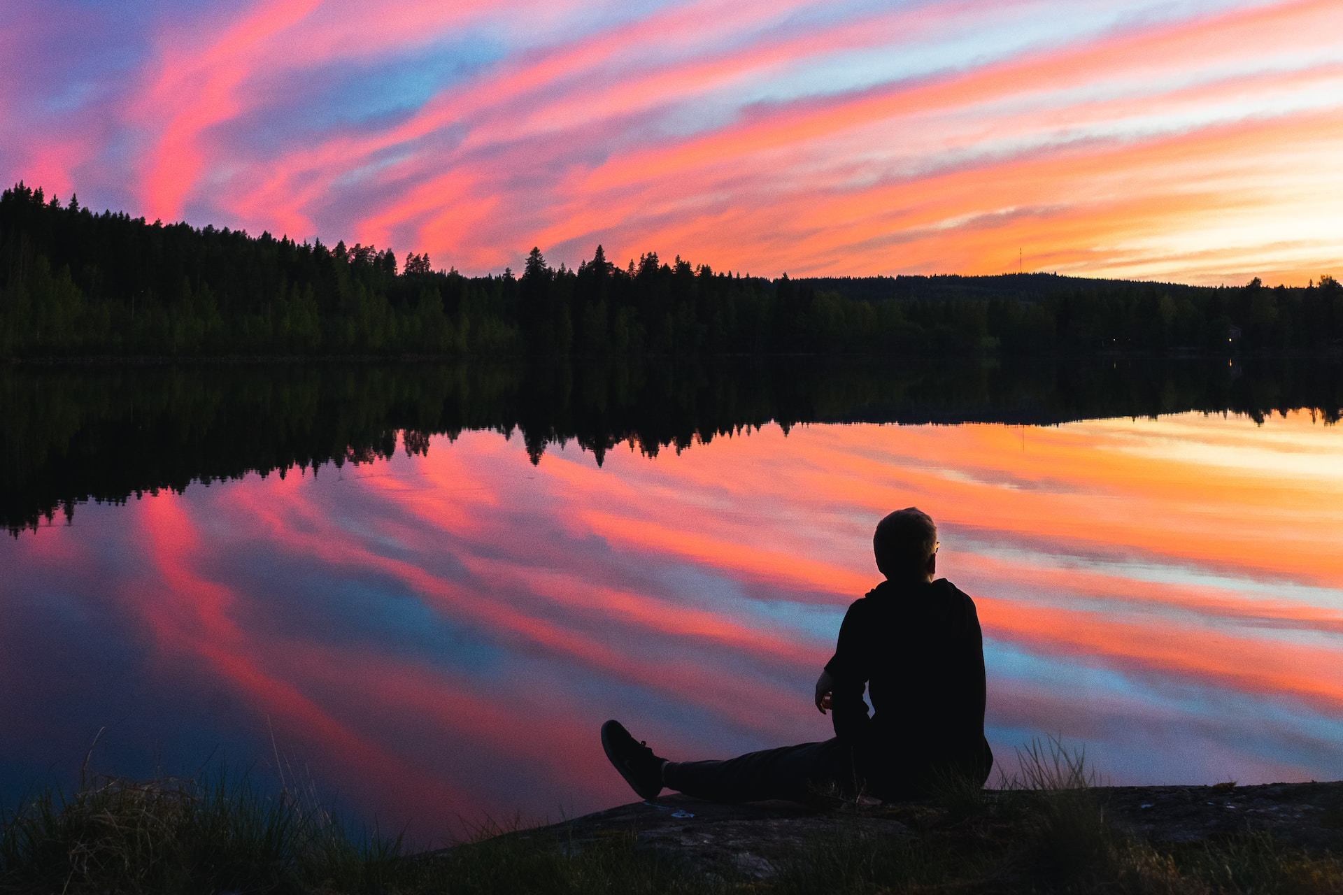 Silhouette of a person sitting by a pond at sunset, with vibrant colors of the sky reflected in the water