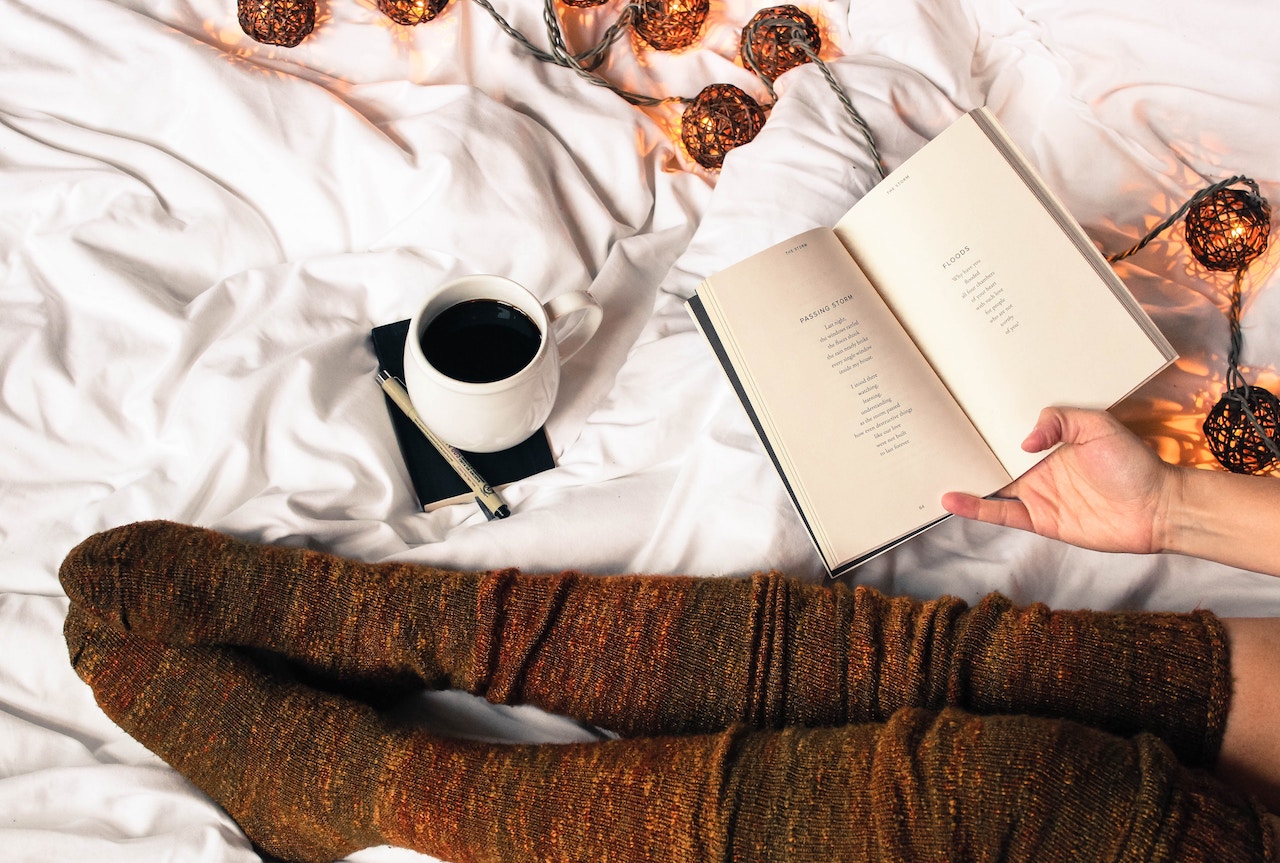 Woman sitting on a bed with coffee and book of poetry