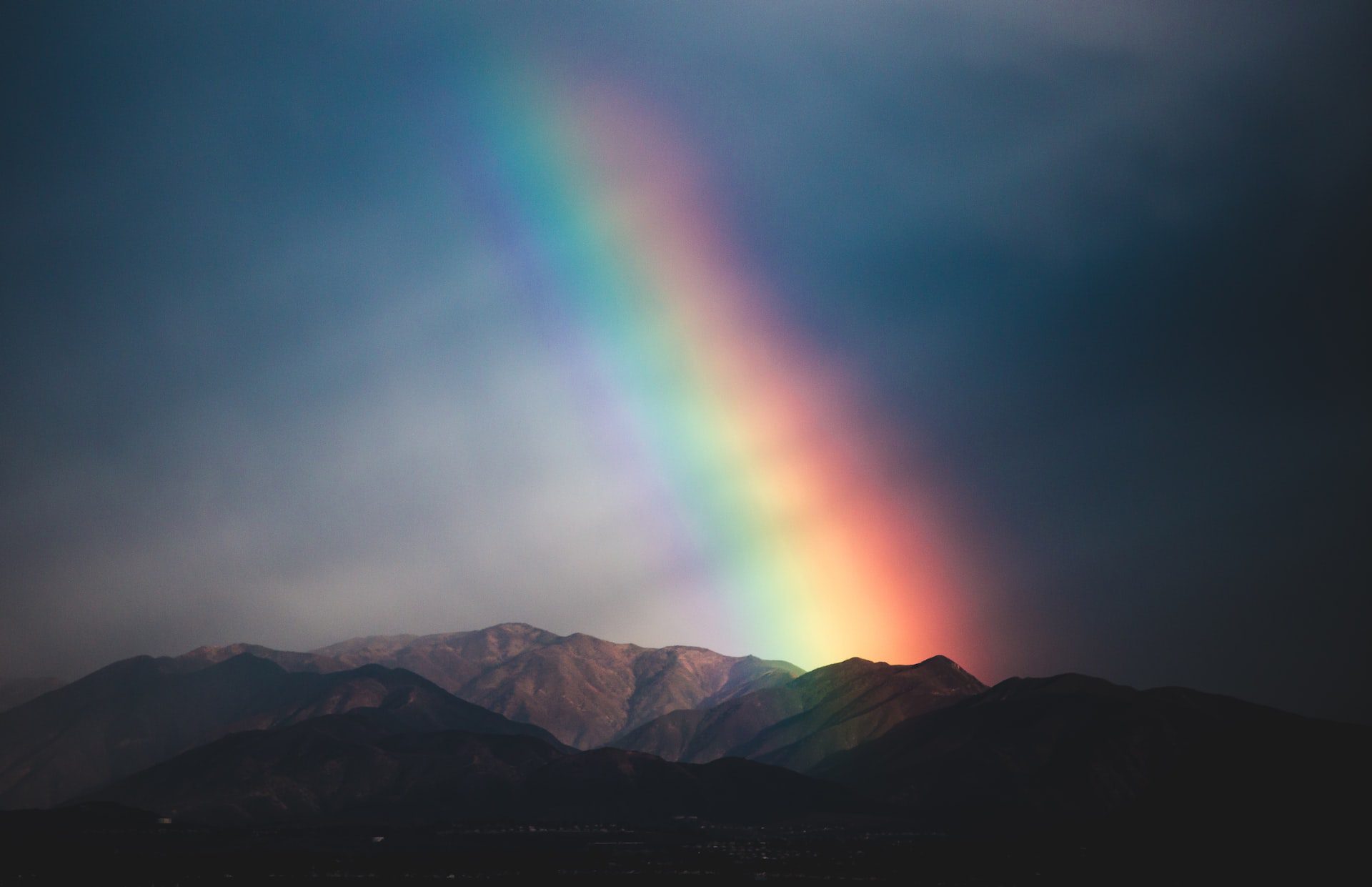 A vibrant rainbow above mountains in a dark sky