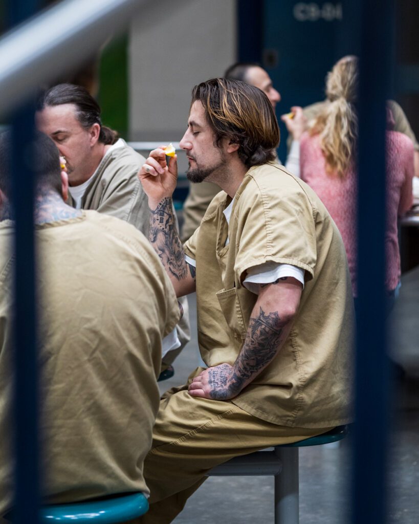 An incarcerated main sits at a table with his eyes closed and deeply inhales the scent of a slice of fruit during a gratitude-focused painting class