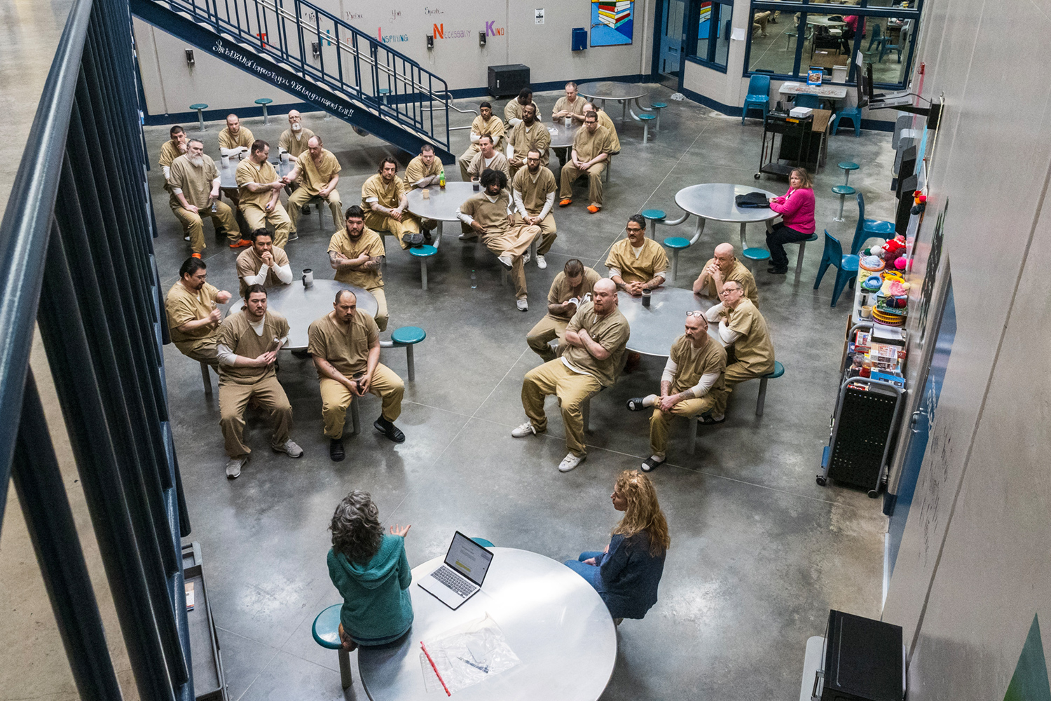 A group of incarcerated men sitting at round tables in a large room for a painting class on gratefulness practices
