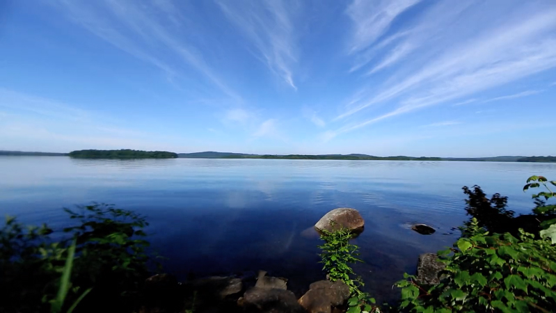 a calm blue lake and blue sky with wispy clouds overhead