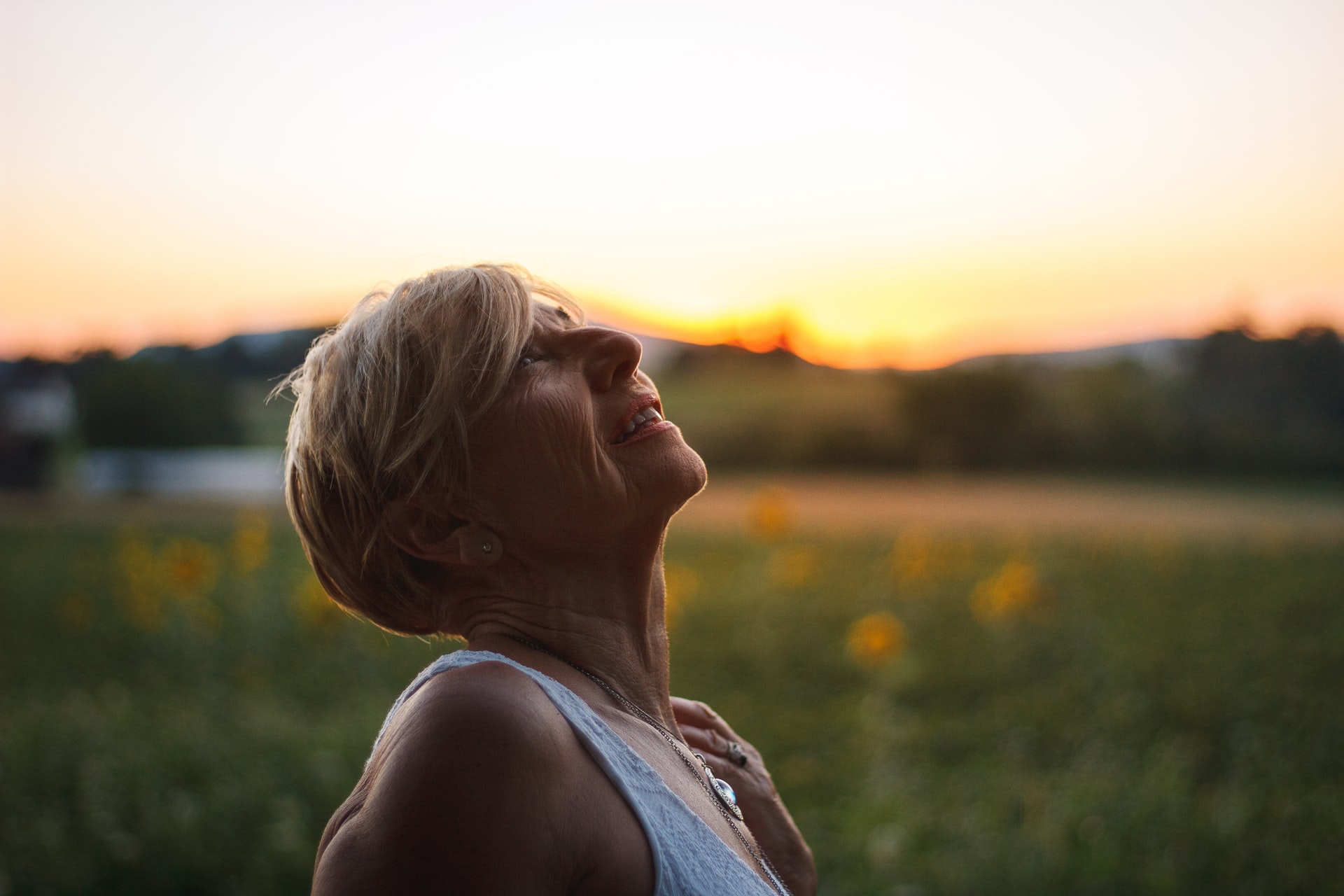 older woman with head tilted back looking up at the sky, with the sunset in the background