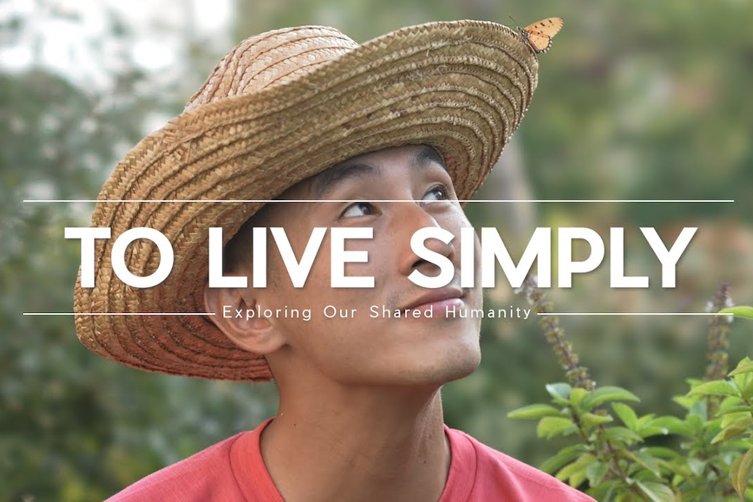 Young man wearing a straw hat looks up to the right at a butterfly sitting on the brim of his hat with text overlay that reads "To Live Simply"