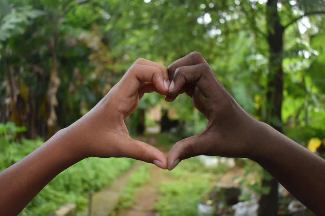 two hands making the shape of a heart with greenery in the background