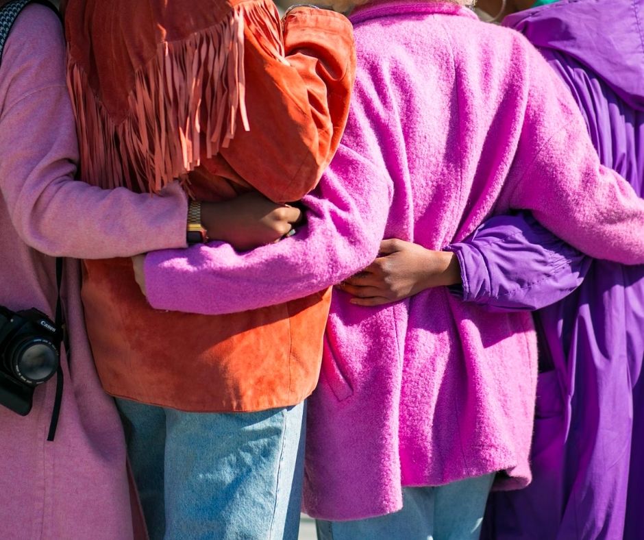 4 people in bright jackets facing away with their arms around each other
