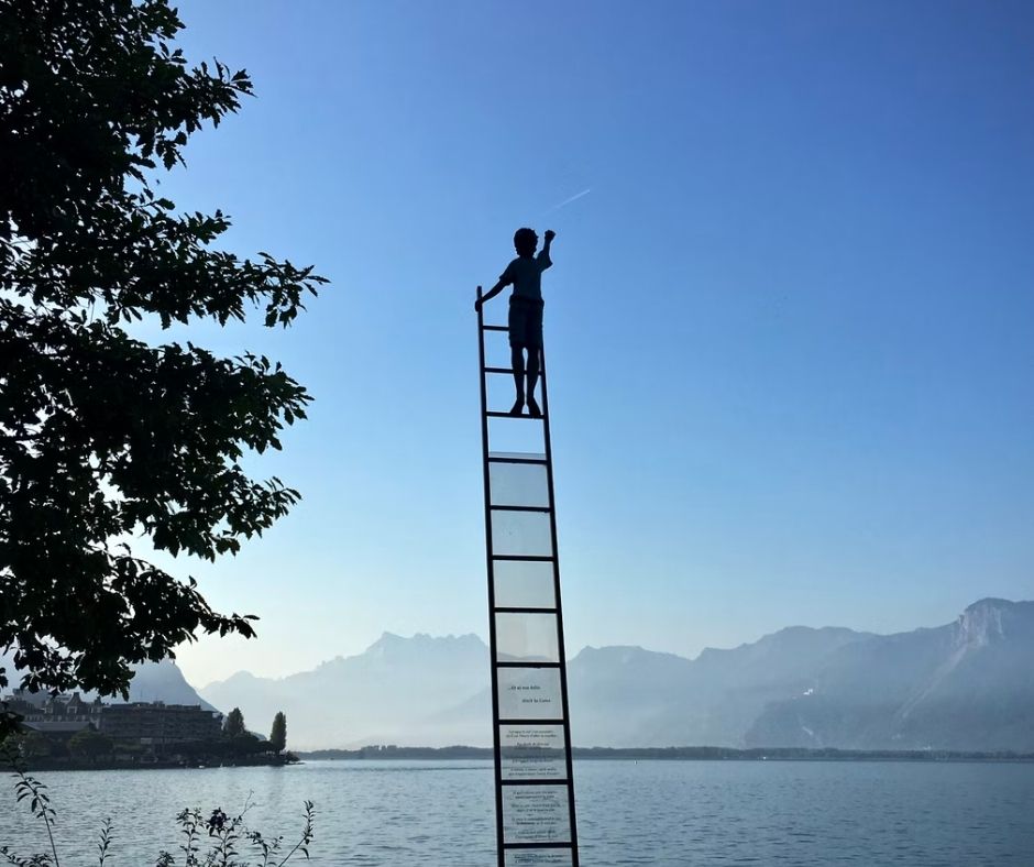 A child at the top of a ladder reaching for the sky