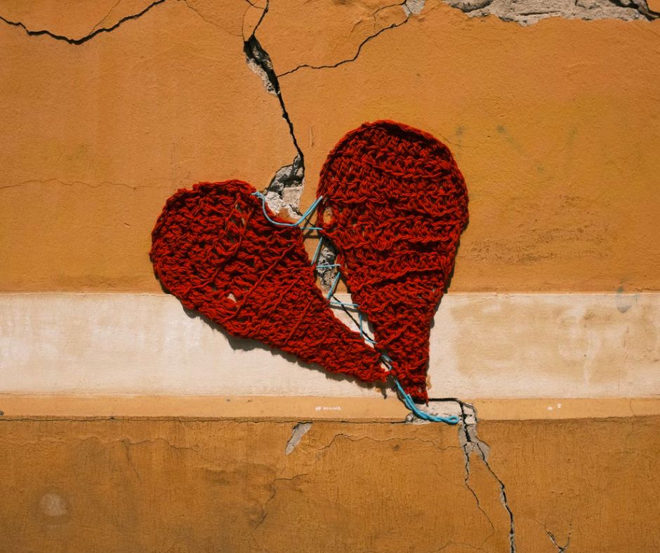 A red knitted heart attached to a crack in a yellow wall
