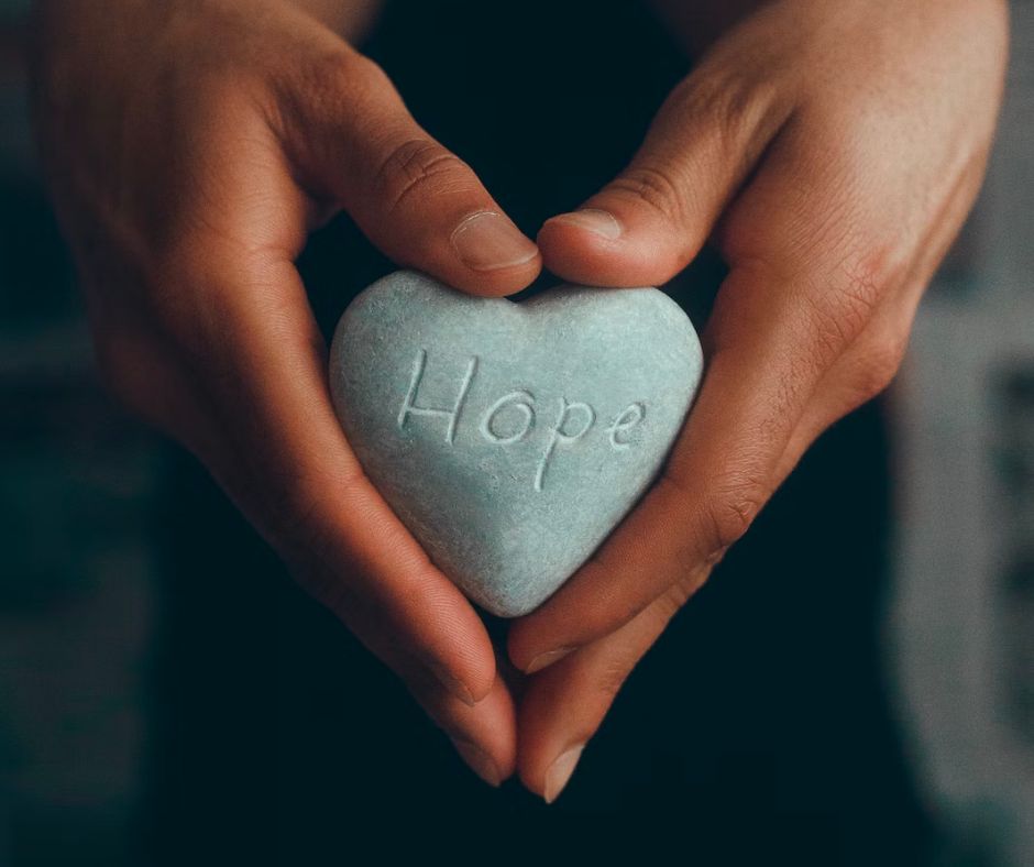 Hands shown holding a heart-shaped stone with "hope" engraved in the center