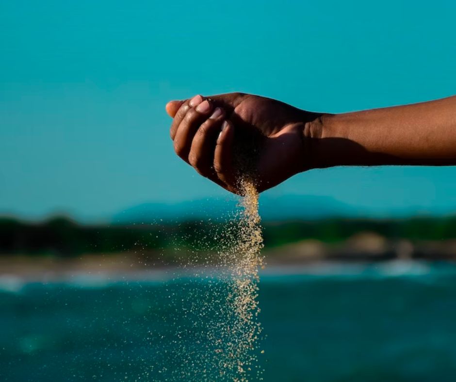 A photo of sand falling out of a hand in front of a backdrop of water