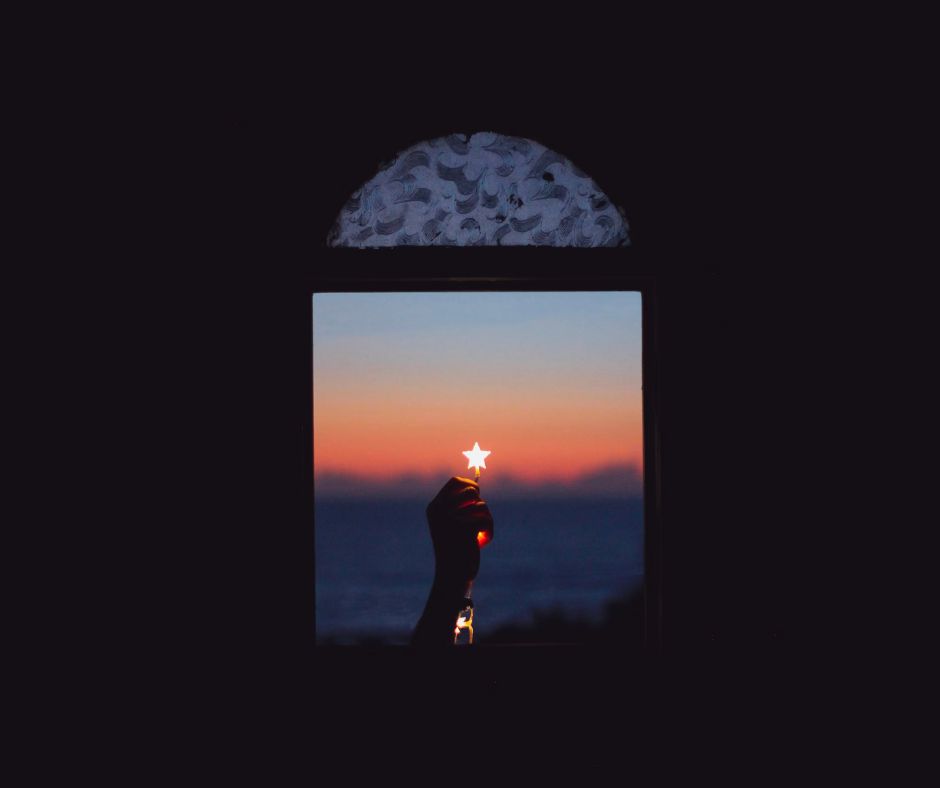 Person holding up a glowing star in a window at sunset