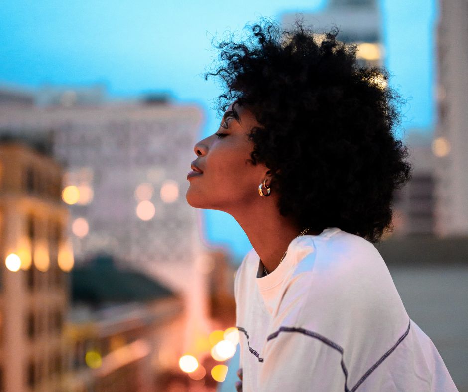A side profile photo of a woman overlooking a city with a serene look on her face