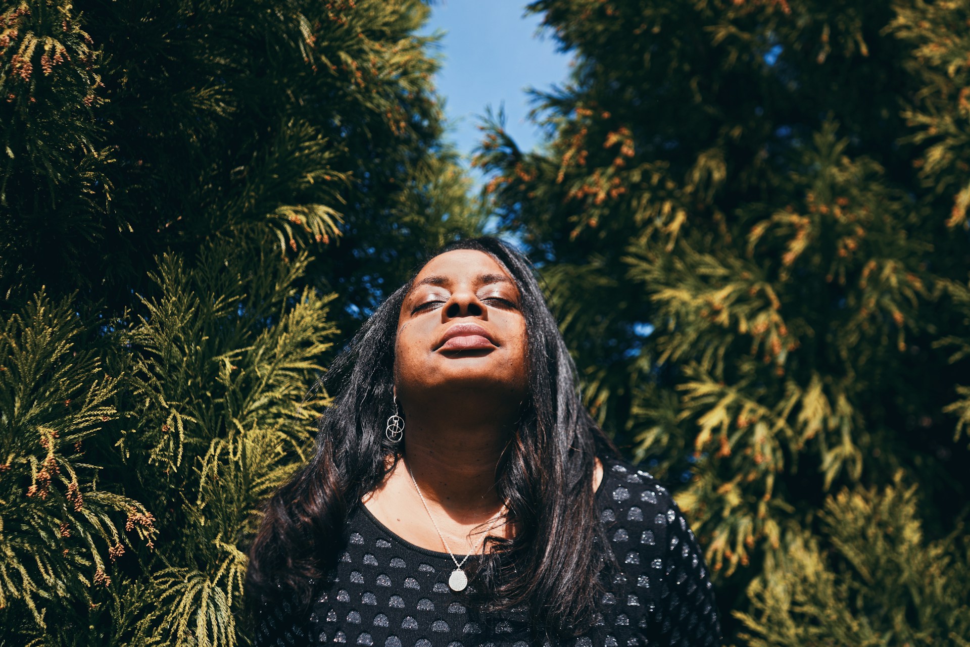 Woman standing still in nature with her eyes closed and face tilted up towards the sun