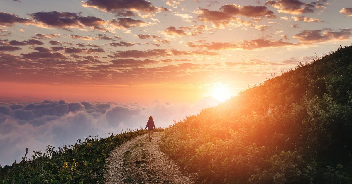 Woman on trail admiring the sunset with clouds and fog.