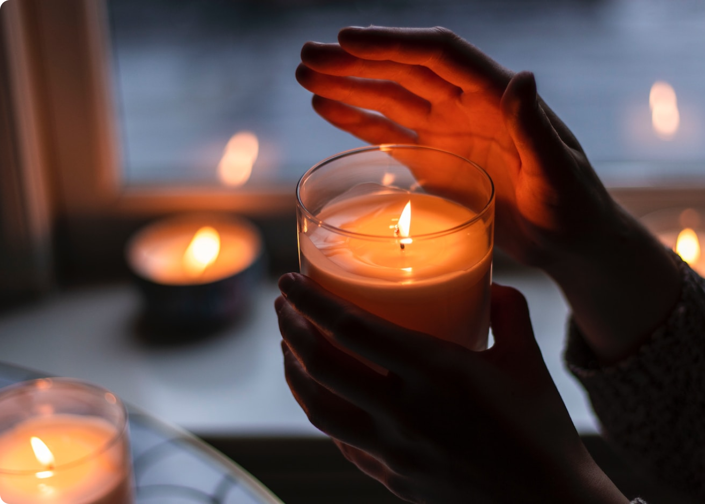 A person holding their hand near a lit candle with others in the background